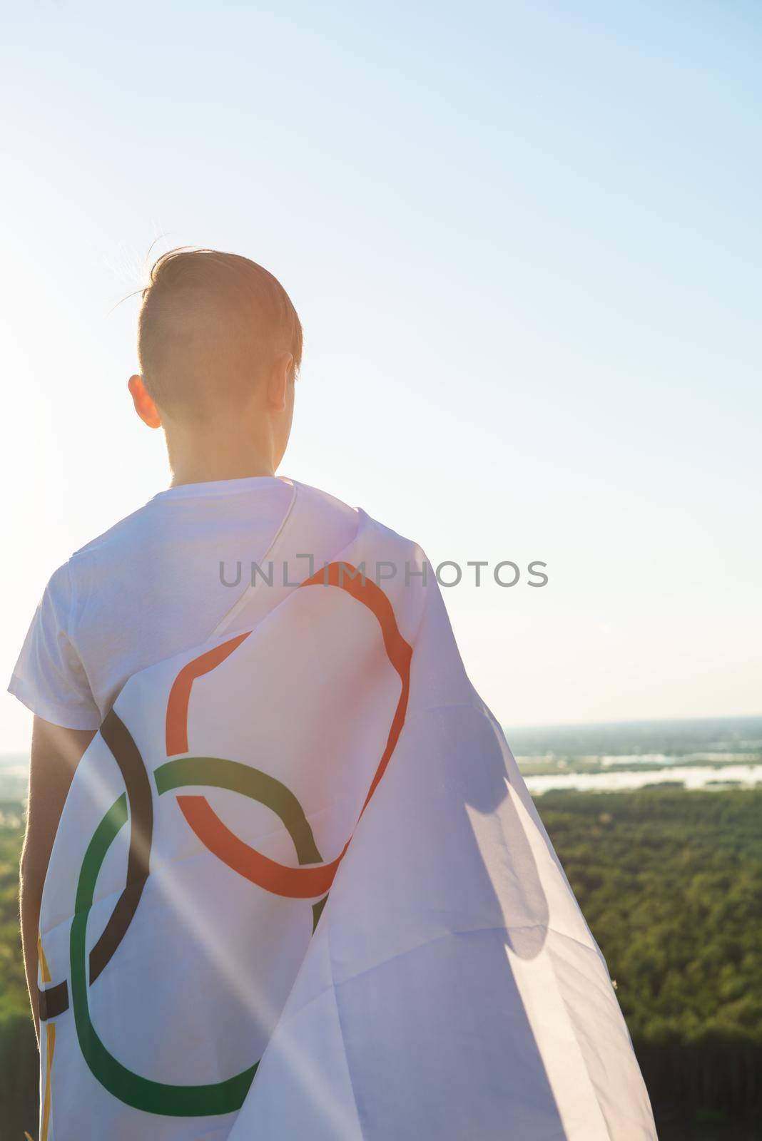 Blonde boy waving waving flag the Olympic Games outdoors over blue sky at the river bank by rusak