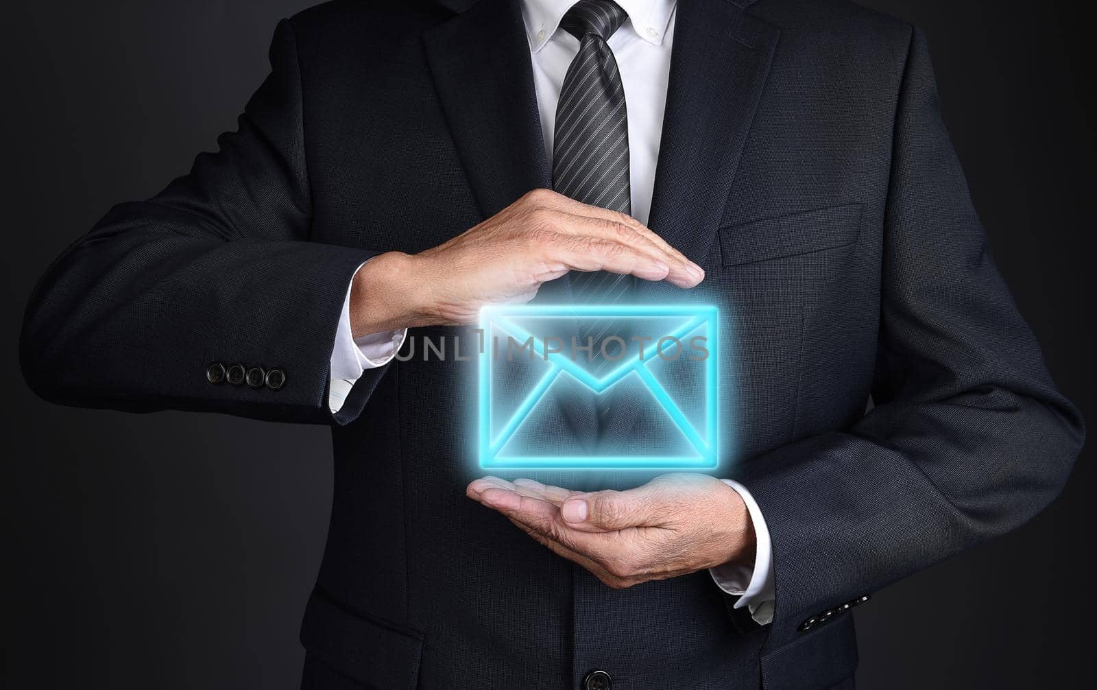 Email Communications Concept. Closeup of an unrecognizable businessman with cupped hands around a neon blue glowing email icon.