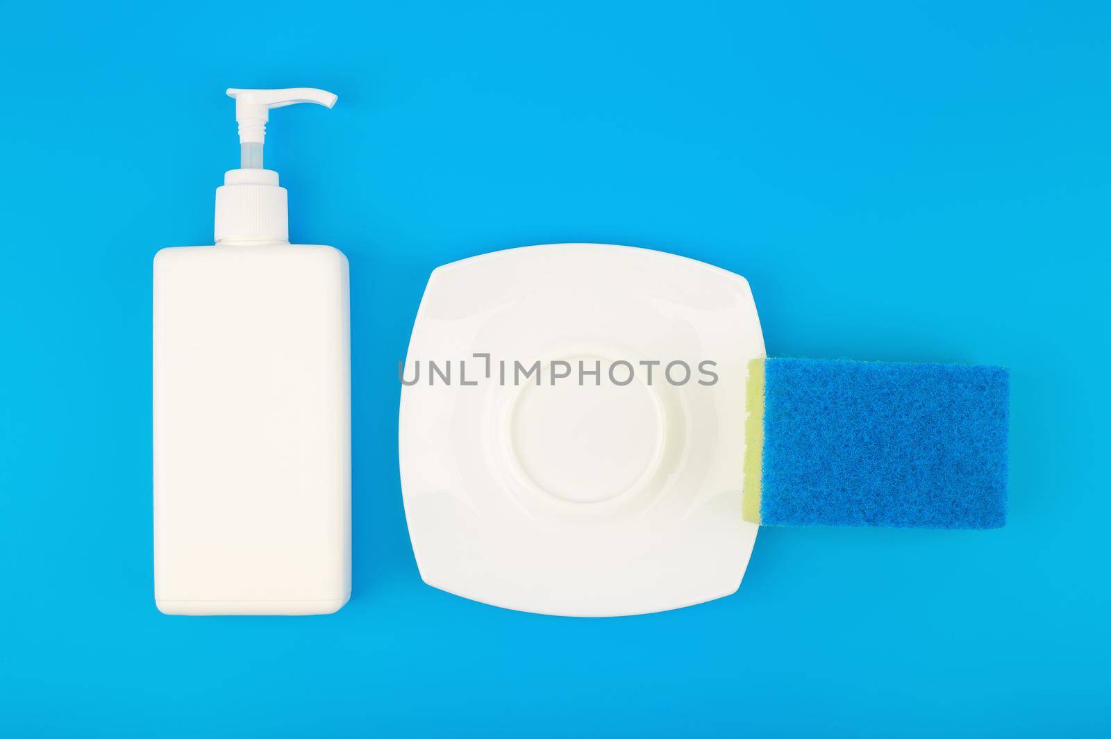 Creative dishwashing concept, top view of detergent, cleaning sponge and clean plate on blue background