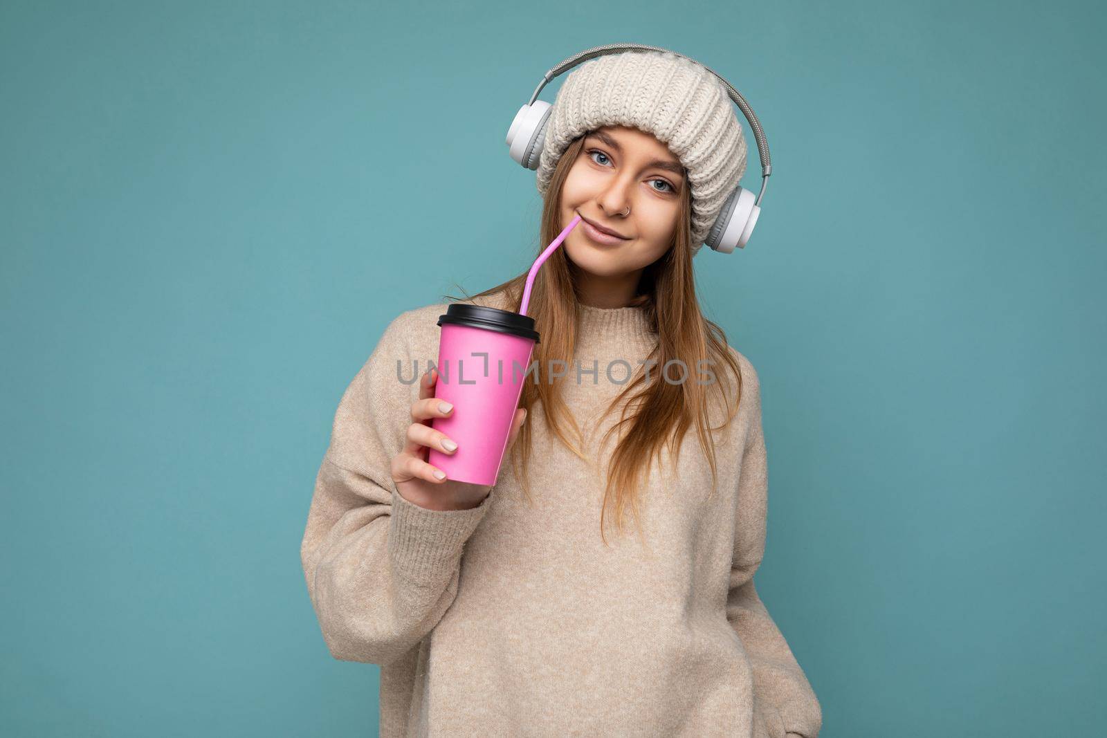 Beautiful young positive blonde woman wearing casual stylish clothes isolated over colorful background wall holding paper cup for mockup drinking coffee looking at camera by TRMK