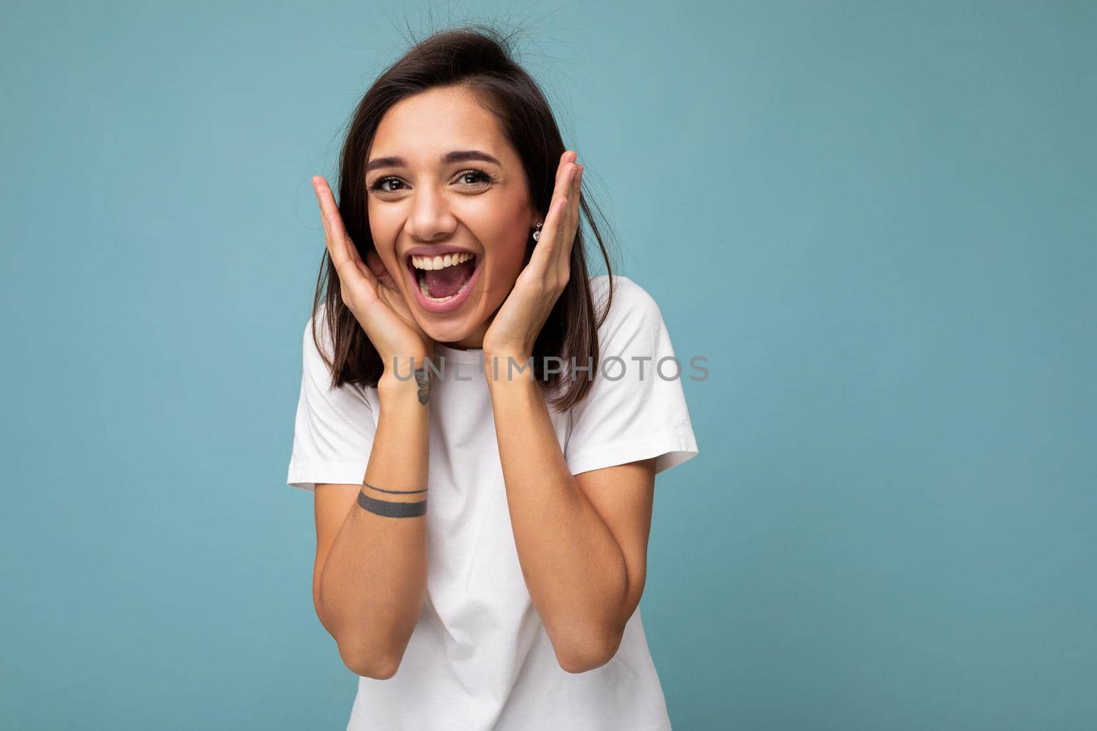 Portrait of happy positive smiling delightful young beautiful brunette woman with sincere emotions wearing casual white t-shirt for mockup isolated on blue background with copy space.