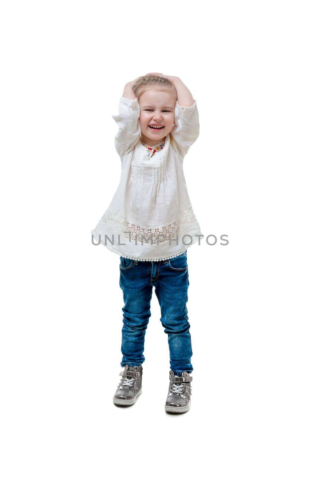 Adorable laughing kid in white sweater and blue jeans, holding her head, isolated
