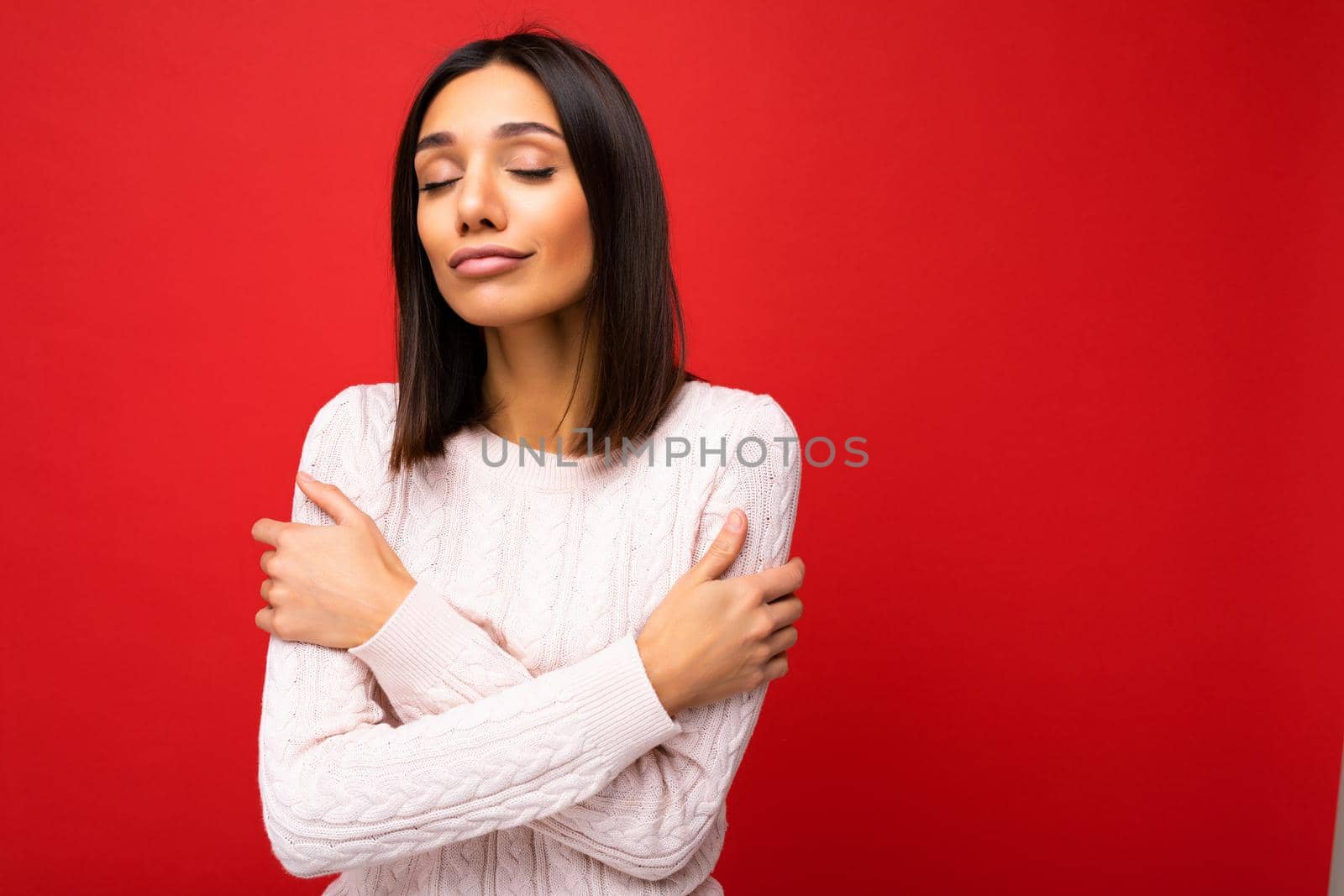 Beautiful cute nice adorable young brunet woman in stylish light knitted jersey isolated over red background wall with free space and enjoying.