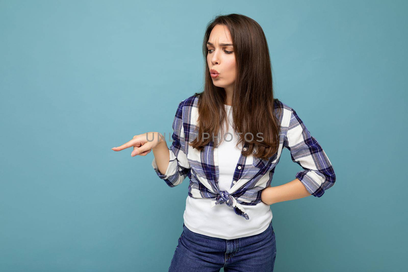 Portrait of beautiful fascinating emotional female promoter pointing to the side at copy space for advertising wearing hipster outfit isolated over background wall with empty space with sincere emotions.