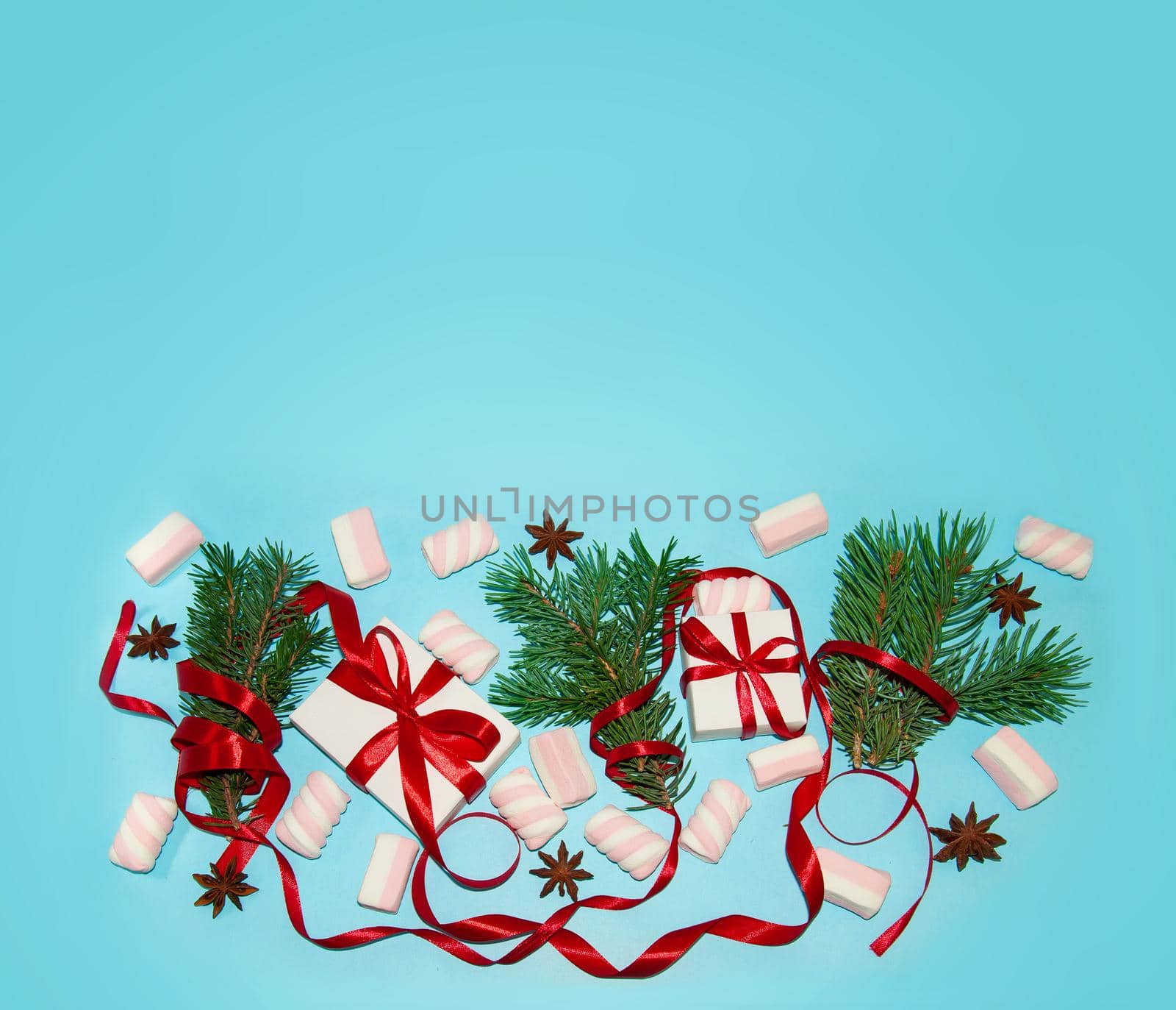 Christmas Holiday Composition. New Year Gift in White Box with Red Ribbon Fir Tree Branches Star Anise Marshmallows on Blue Background Flat Lay Top View with Copy Space For Your Text