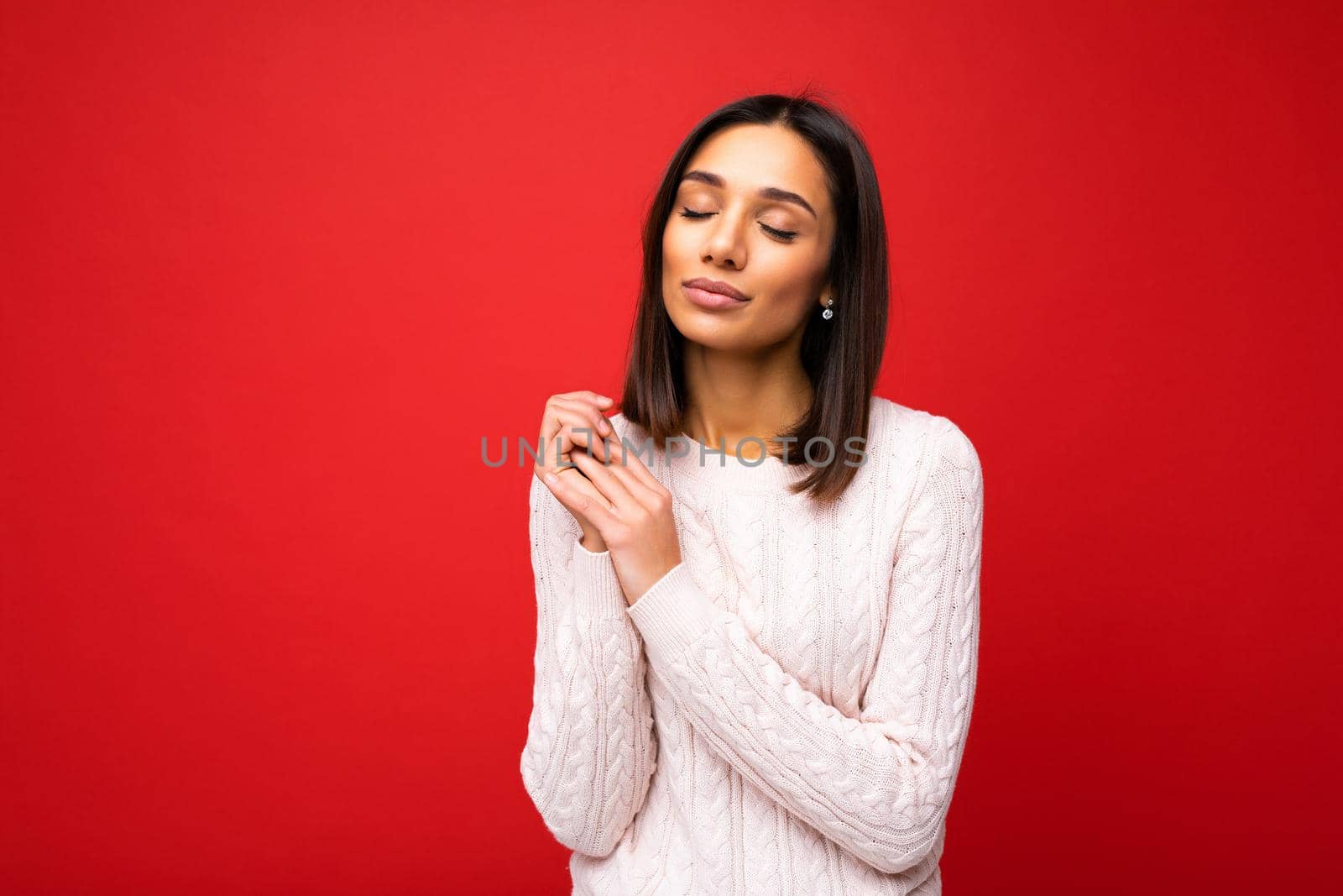 Attractive cute nice adorable tender young brunette woman in casual light knitted sweater isolated on red background with free space and enjoying.