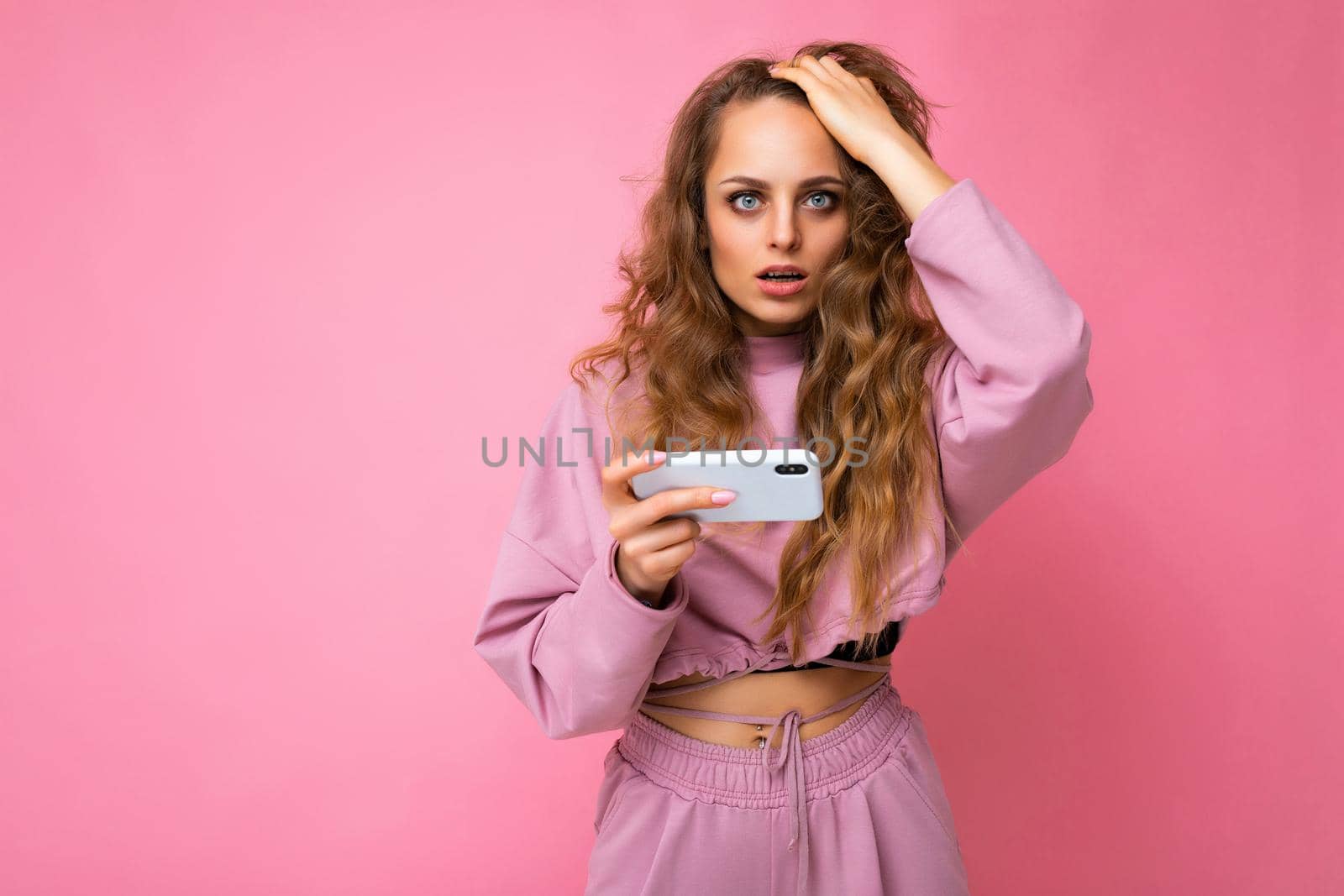 Photo of attractive crazy amazed surprised young woman wearing casual stylish clothes standing isolated over background with copy space holding and using mobile phone looking at camera.