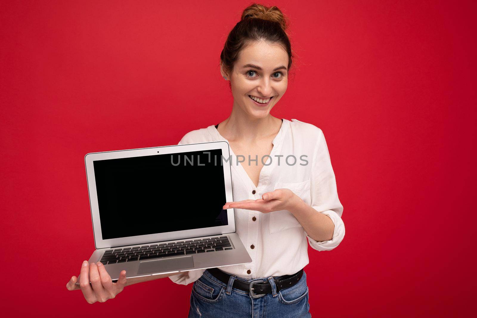 Close-up portrait of Beautiful smiling happy young woman holding computer laptop looking at camera having fun wearing casual smart clothes isolated over red wall background. cutout