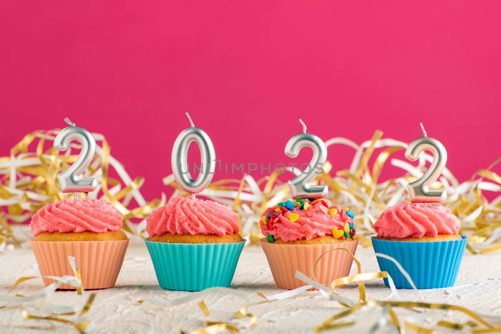 Festive cupcakes and candles in form of numbers 2022 on pink background. Concept of New year