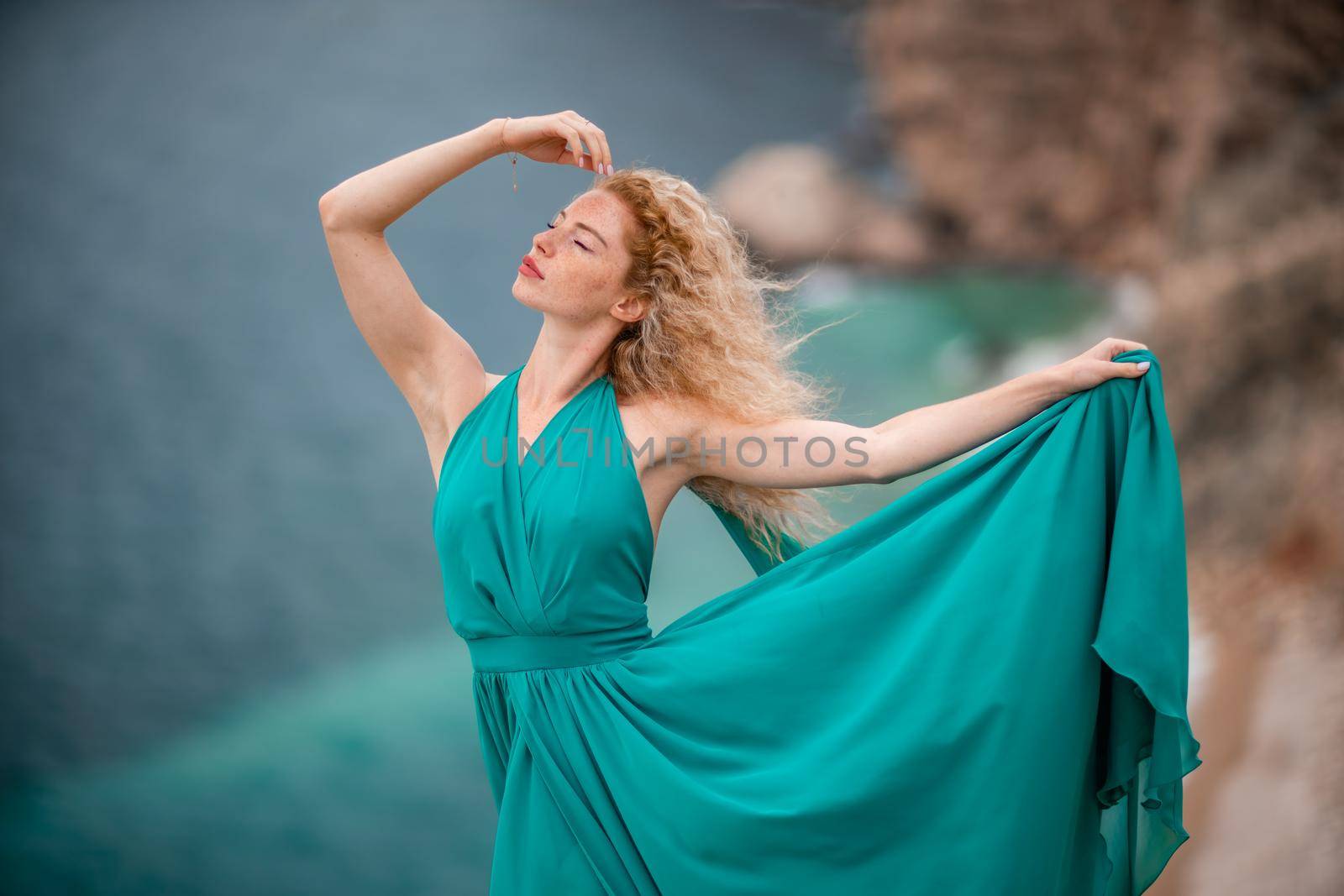 A woman in an emerald dress, a fashion model with long silk wings in a flowing dress, flying fabric on the embankment