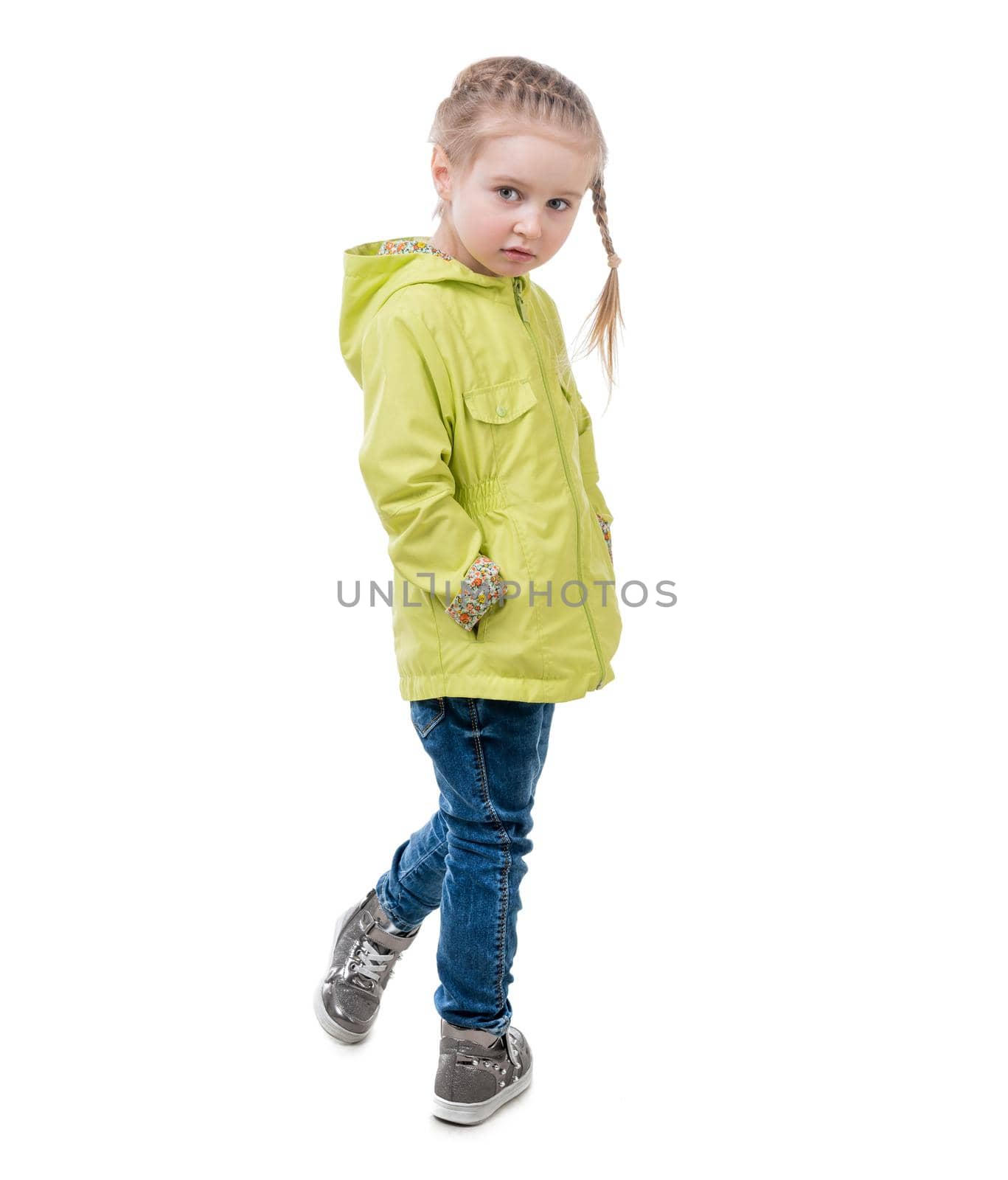 Adorable girl in yellow coat, standing turned, hands in pockets, isolated on white background