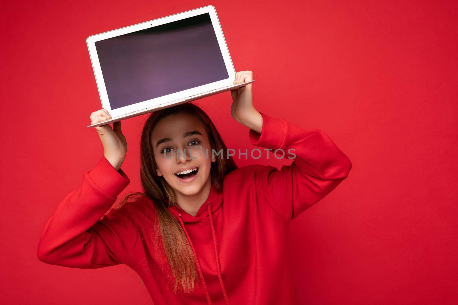 Photo of beautiful young girl holding computer laptop looking at camera isolated over colourful background.