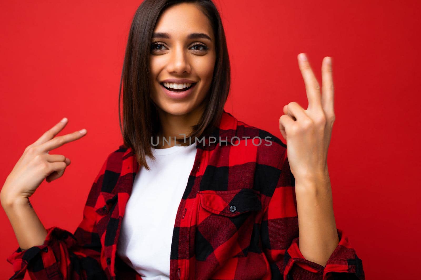 Closeup of young happy positive cool pretty brunette woman with sincere emotions wearing white t-shirt and trendy red check shirt isolated on red background with free space and having fun.