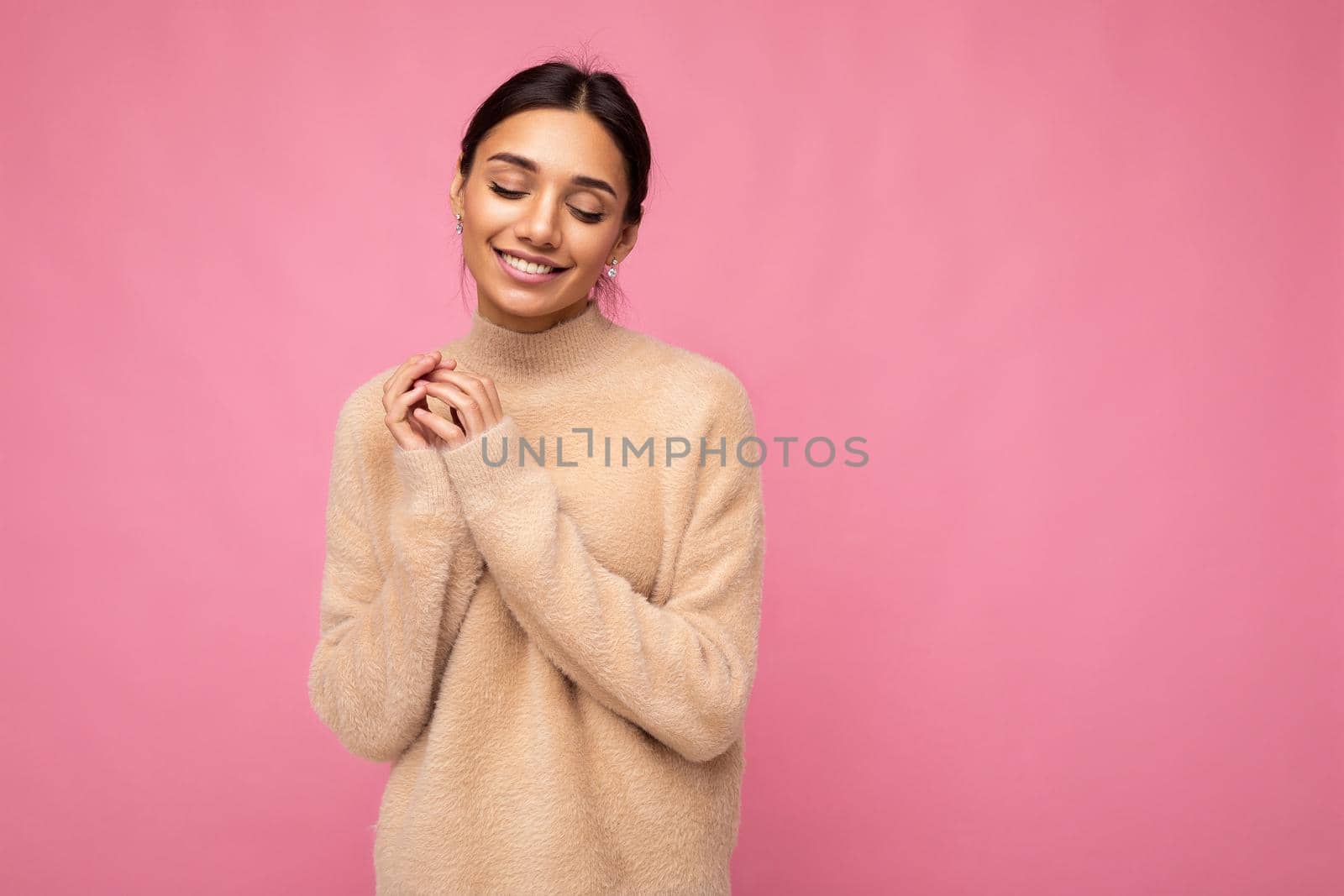 Photo of young beautiful happy smiling brunette woman wearing beige jersey . Sexy carefree female person posing isolated near pink wall in studio with free space. Positive model with natural makeup.