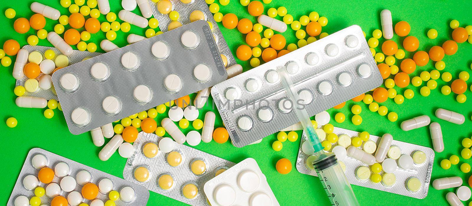 colorful and white pills, capsules, syringe. Prevention, cure of influenza, coronavirus, covid-19. yellow, orange vitamins, tablets on green background. medical healthcare, protection concept banner