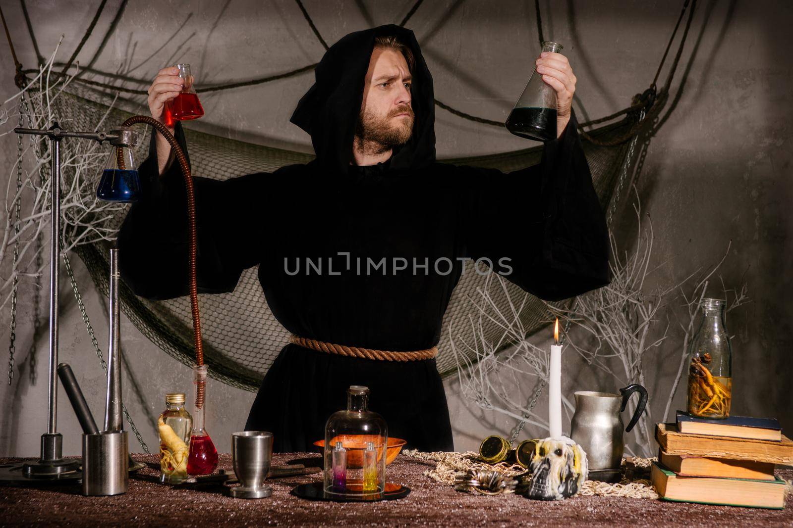 medieval alchemist scientist magician looks at the flasks in his laboratory. Halloween concept. The bearded man in the mantle