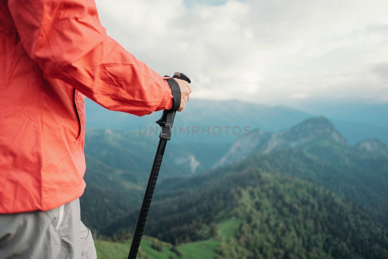 Unrecognizable hiker young woman with trekking poles walking in summer mountains.