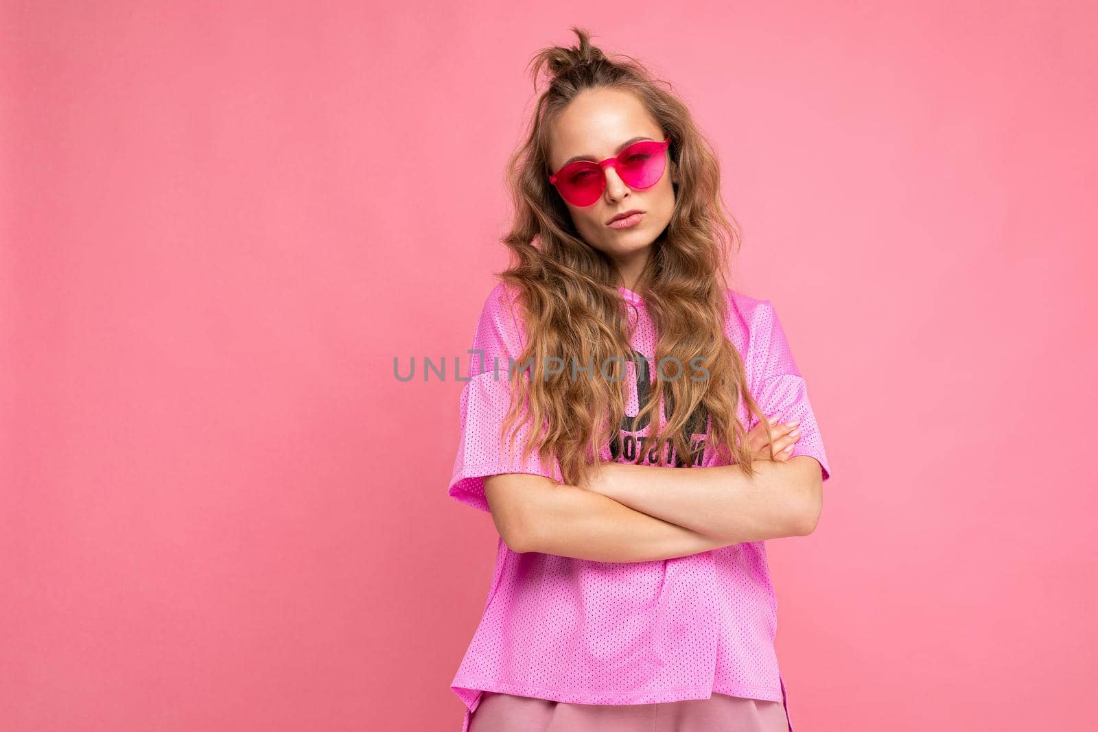 Photo shot of beautiful young dark blonde woman wearing casual clothes and stylish sunglasses isolated over colorful background looking at camera.