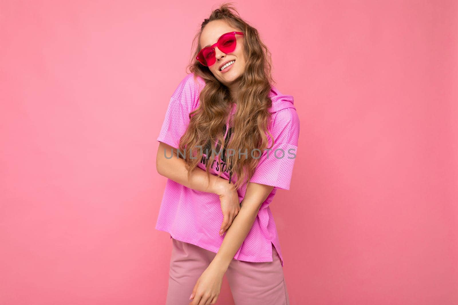 Photo shot of beautiful young dark blonde woman wearing casual clothes and stylish sunglasses isolated over colorful background looking at camera.