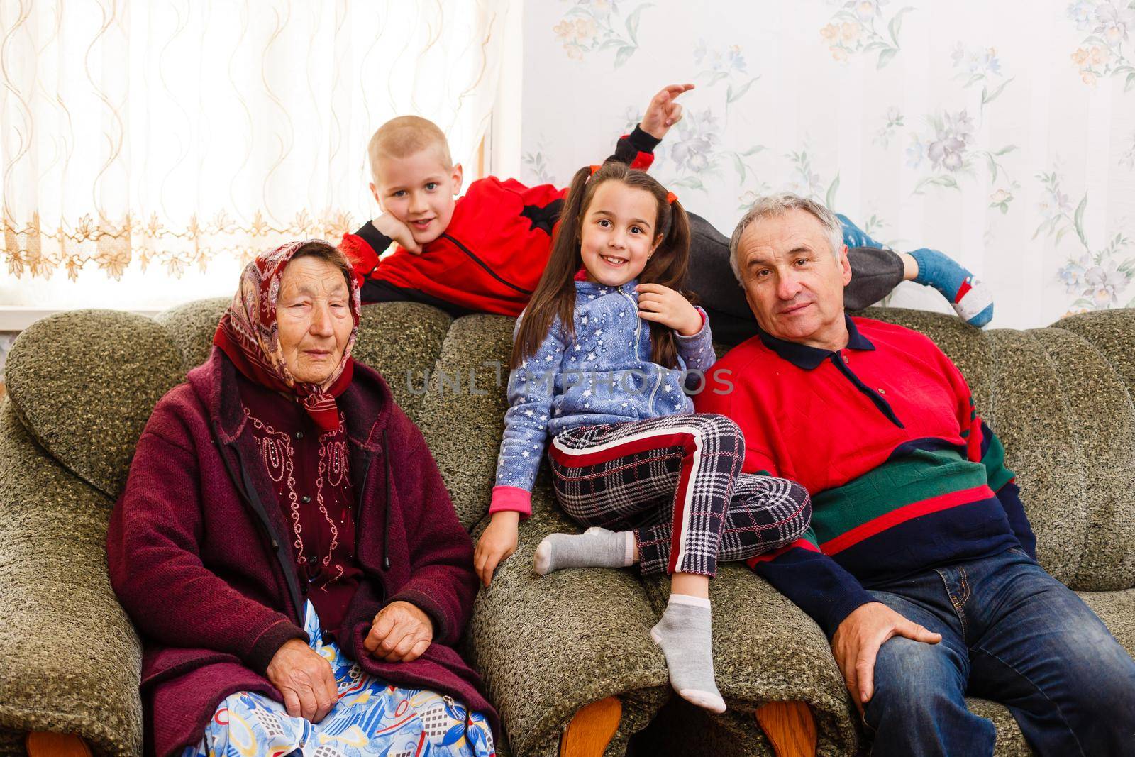 Happy young boy and girl with their laughing grandparents smiling at the camera as they pose together indoors by Andelov13