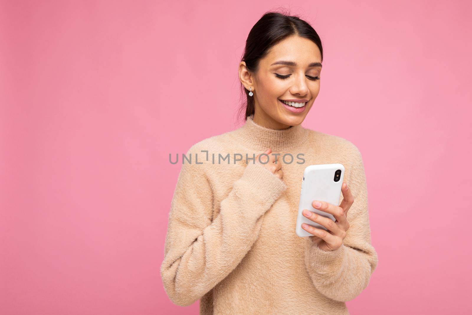 Young woman over isolated pink background sending a message with the mobile.
