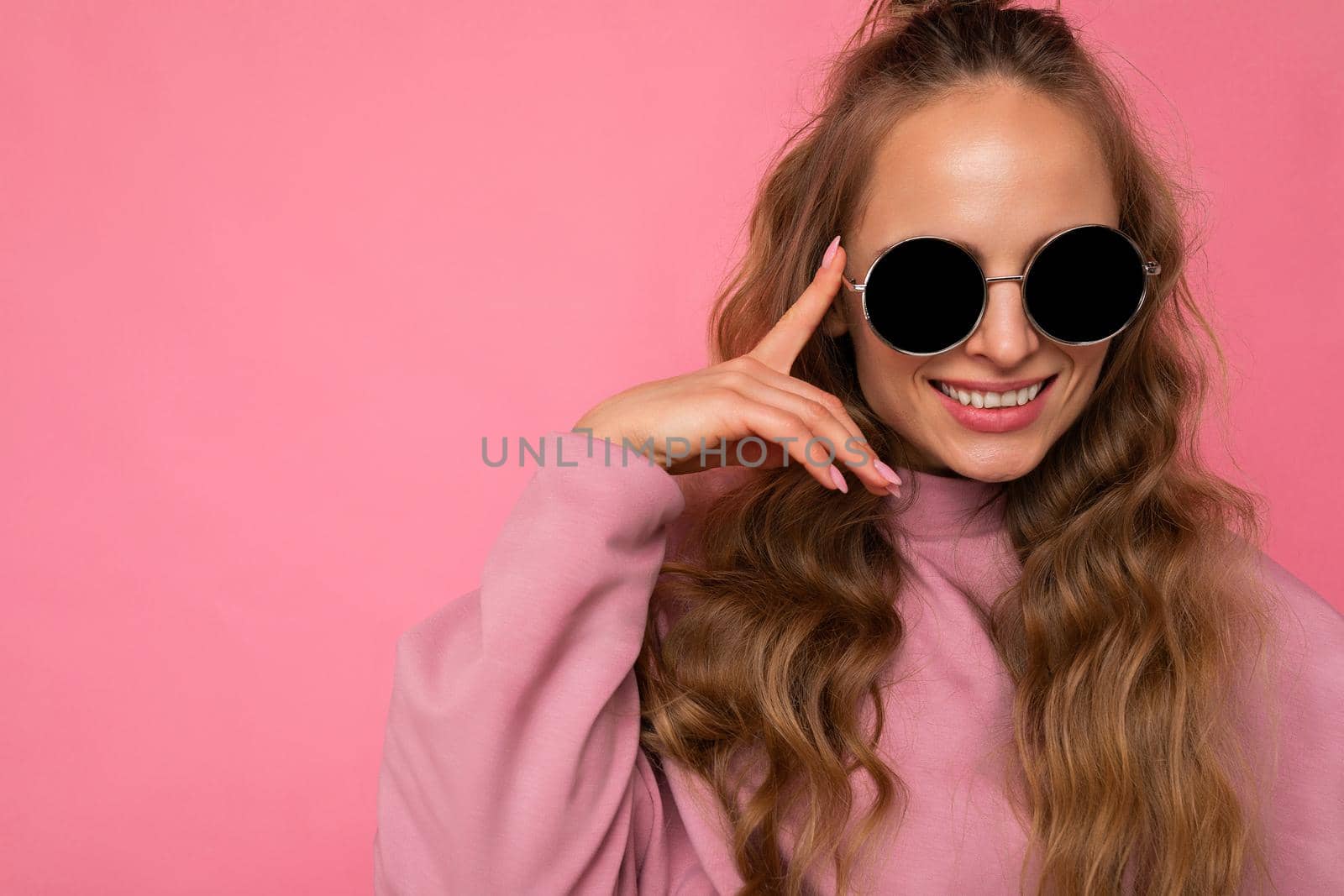 Closeup photo of pretty positive smiling young blonde curly woman isolated over pink background wall wearing casual pink sport clothes and stylish sunglasses looking at camera. copy space