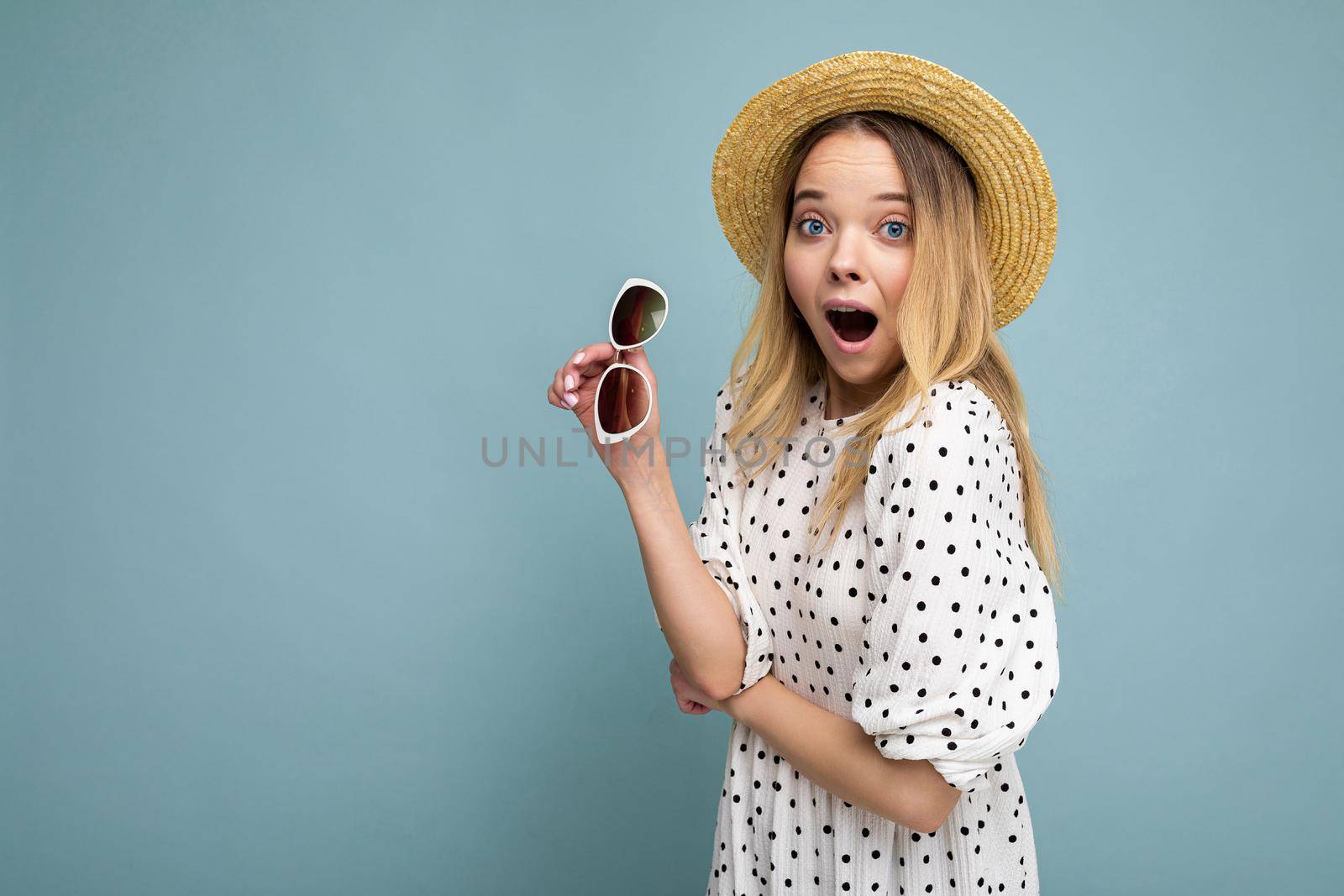 Attractive shocked young blonde woman wearing everyday stylish clothes and modern sunglasses isolated on colorful background wall looking at camera with open mouth. copy space