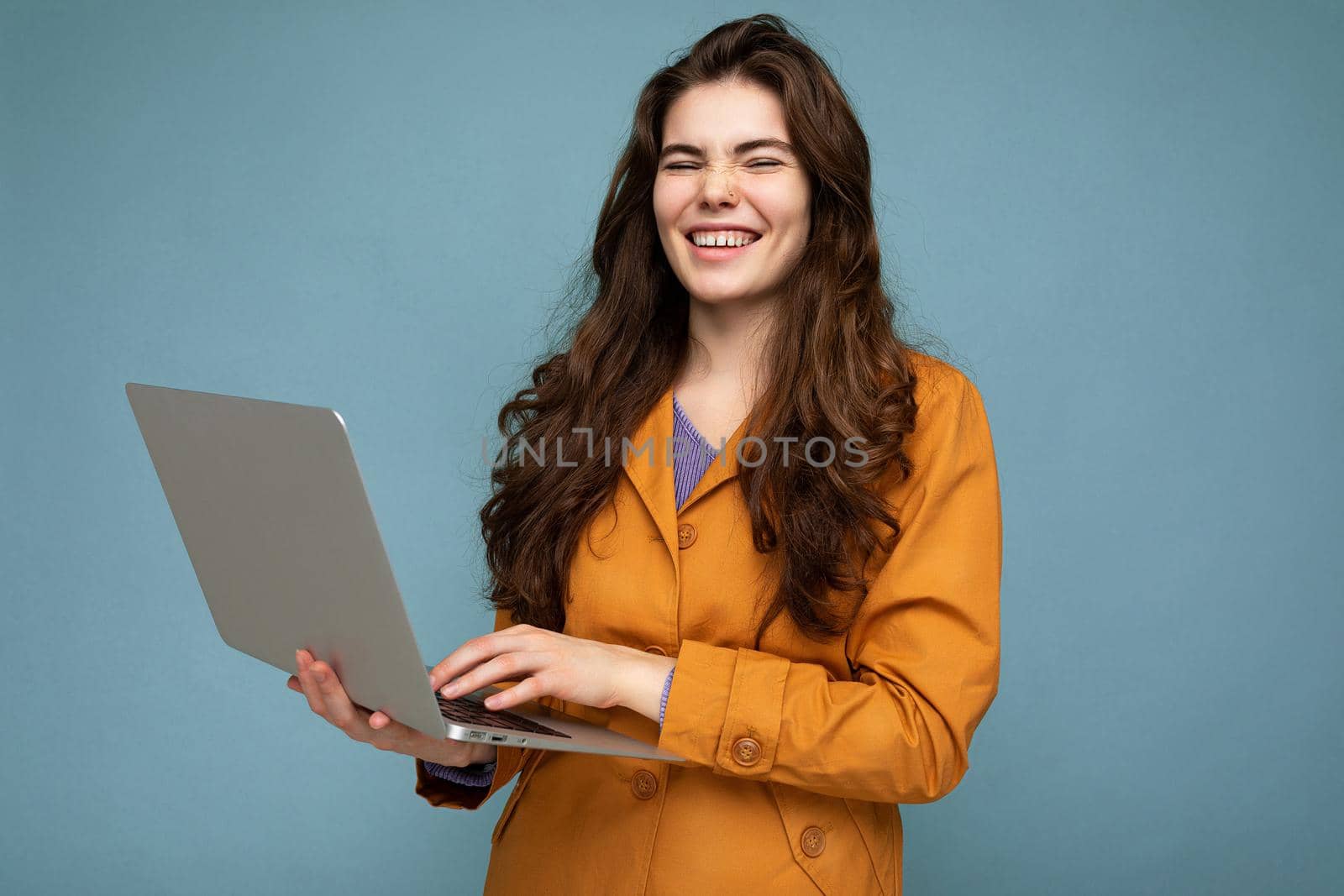 Photo of beautiful young woman holding computer laptop looking at camera isolated over colourful background.