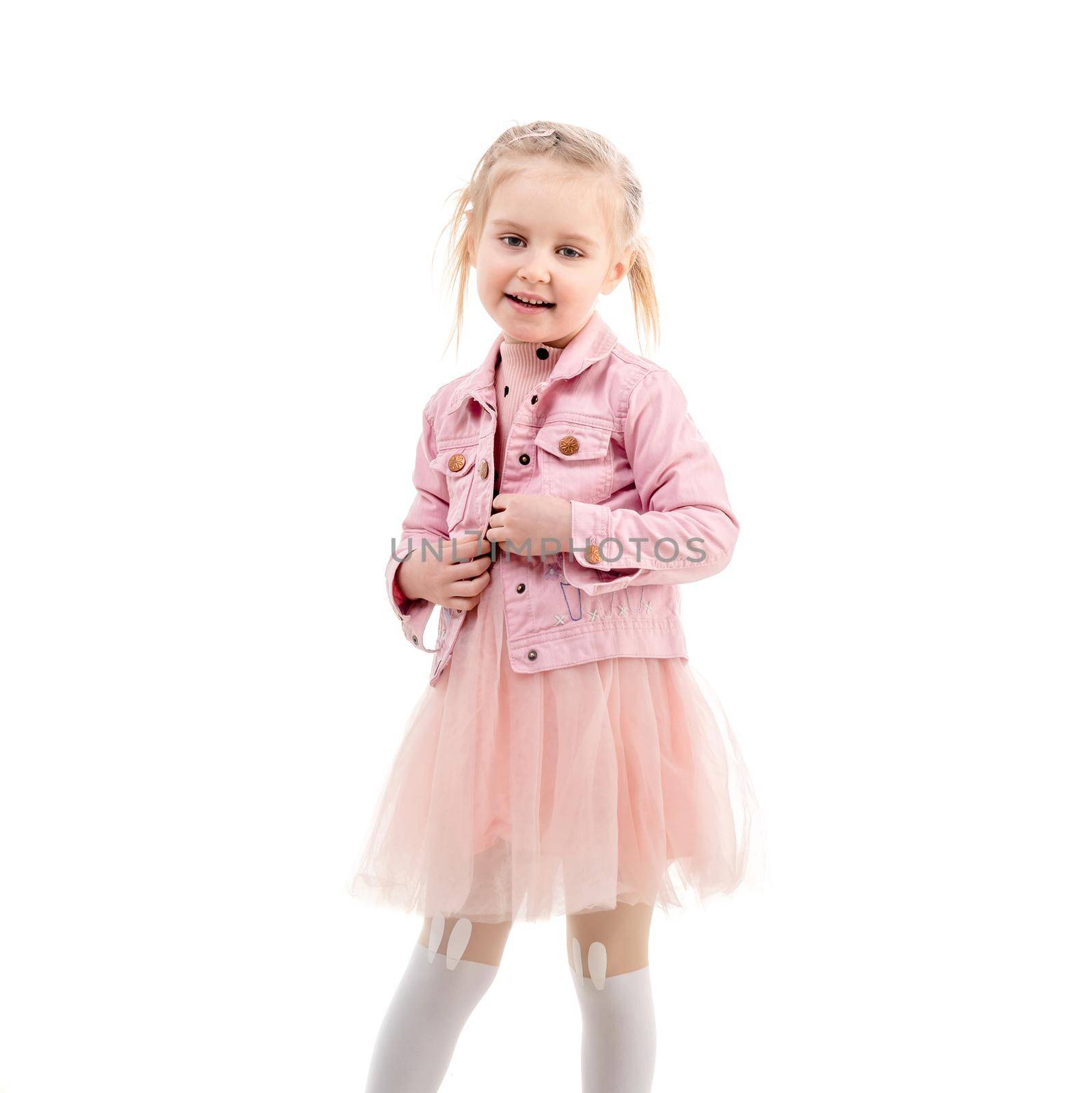 Sweet kid smiling and holding her pink jacket, wearing puffy skirt and white stockings, isolated