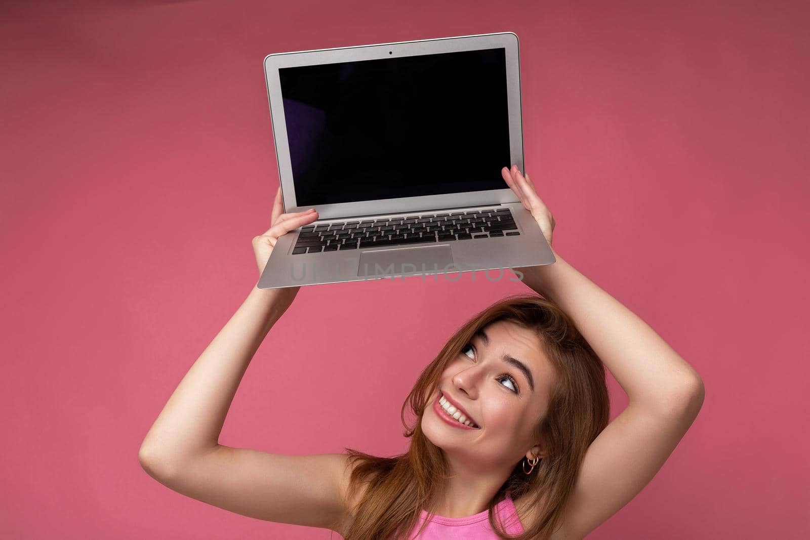 Side profile portrait of overjoyed Beautiful smiling happy young woman holding computer laptop looking up at netbook montor having fun wearing casual smart clothes isolated over wall background. Empty space, free space for advertising