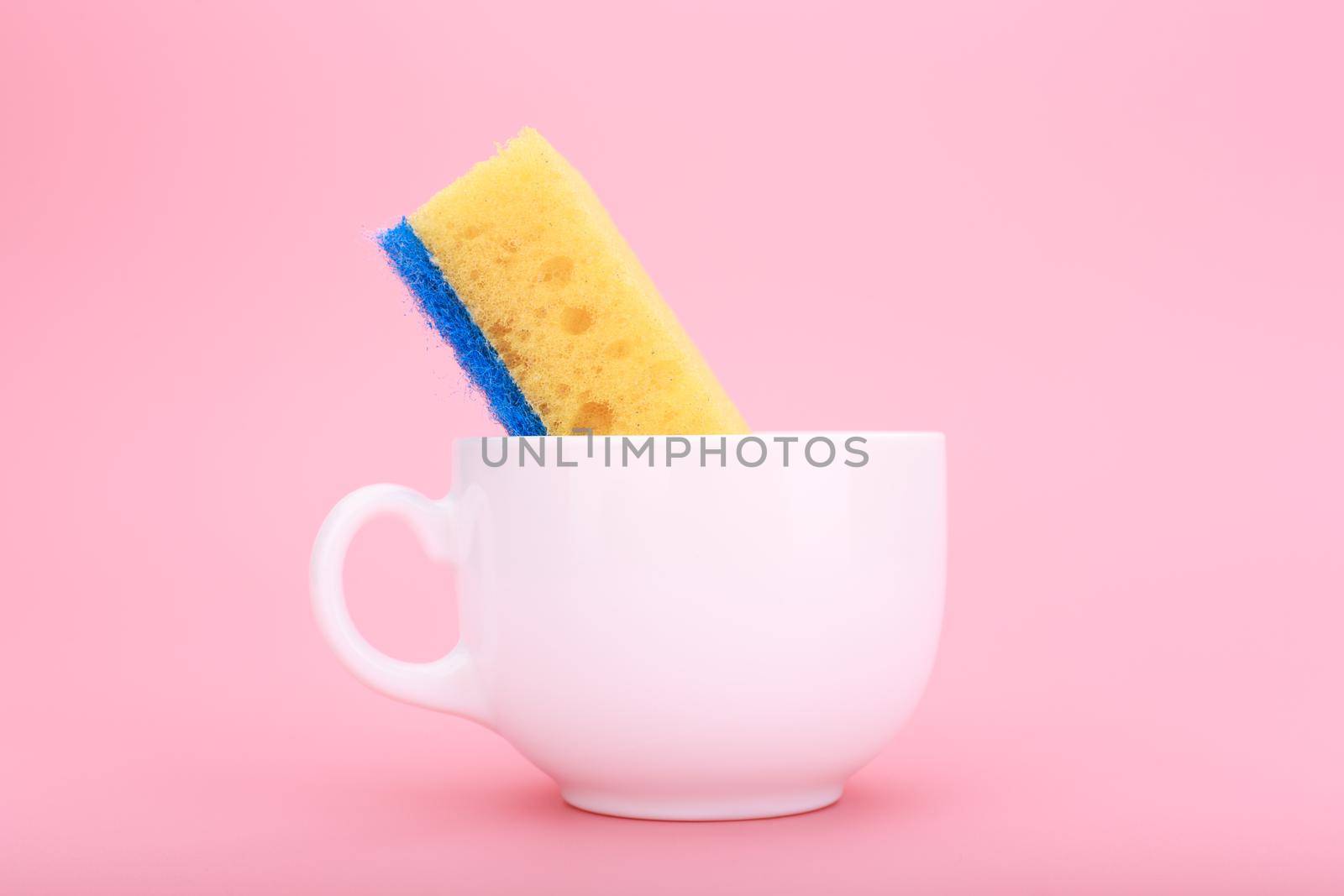 Creative, minimal dishwashing concept. Simple composition with yellow cleaning kitchen sponge in white ceramic cup on pink background