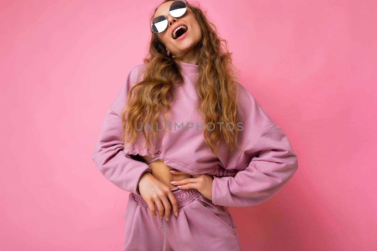 Photo of pretty positive young blonde curly woman isolated over pink background wall wearing casual pink sport clothes and stylish sunglasses looking up by TRMK