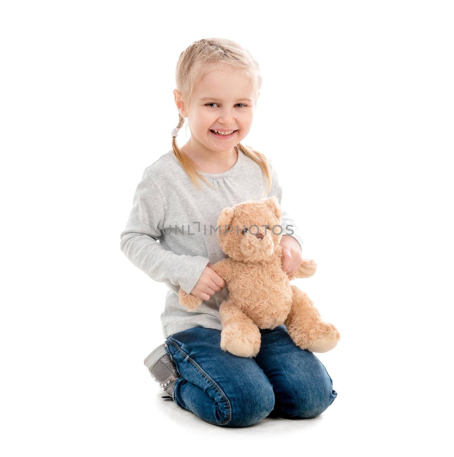 Kid sitting and hugging her favorite teddy toy, lovely hairstyle, isolated on white background