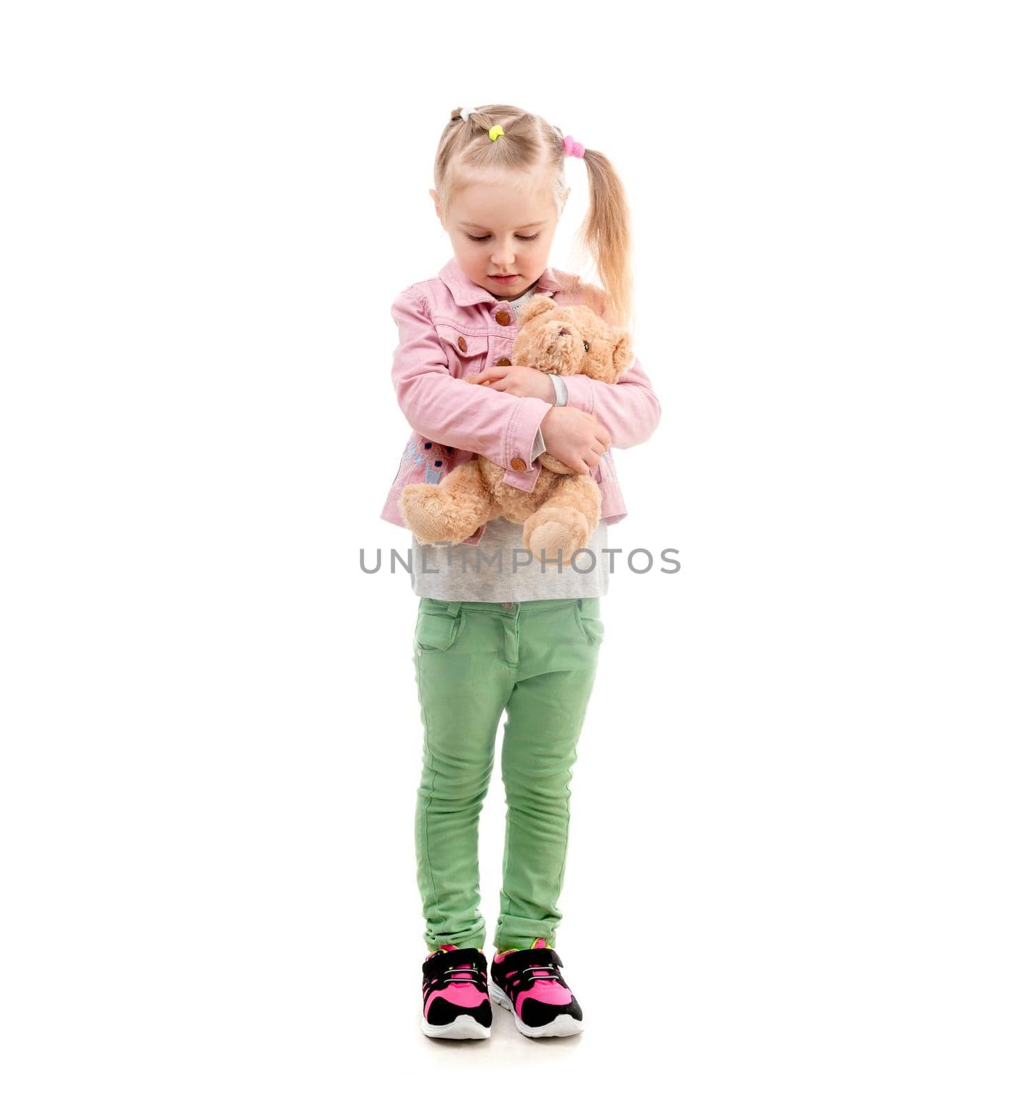 Lovely girl in pink jacket standing and hugging her toy, isolated on white background
