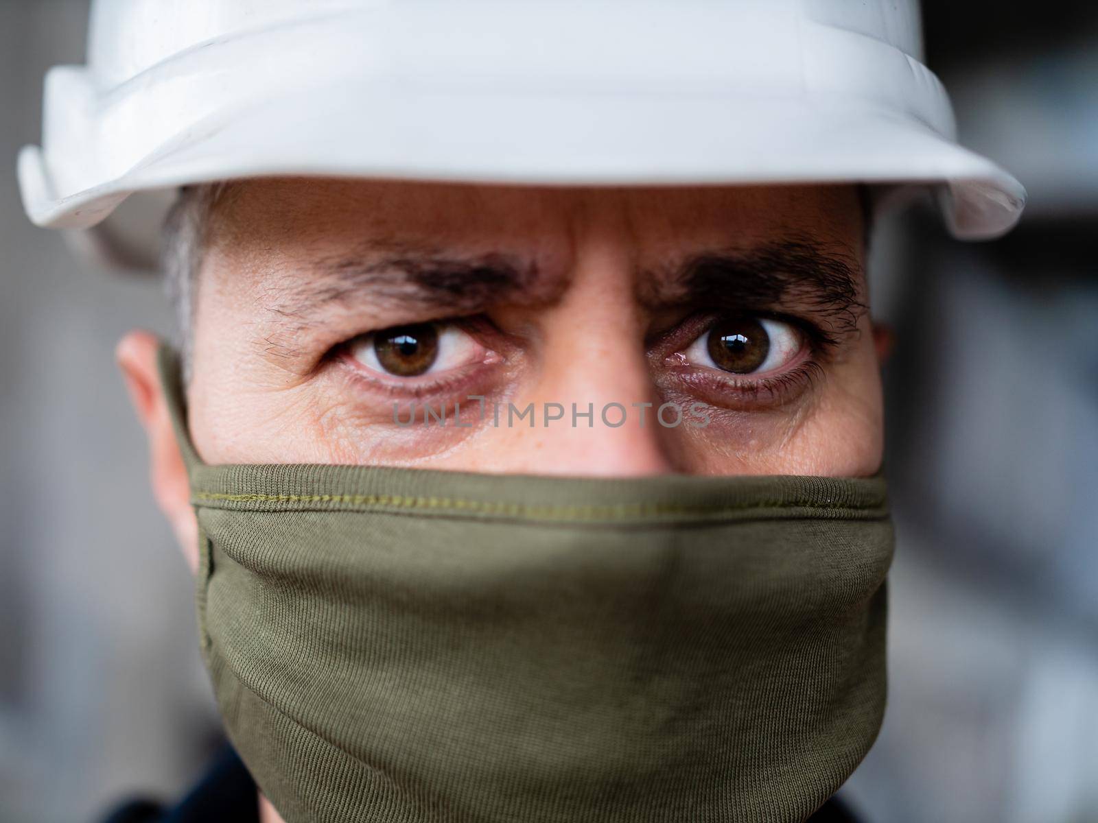 Portrait of foreman wearing mask and hardhat at construction site, building in background. Concept of coronavirus social distance and covid-19. by Utlanov