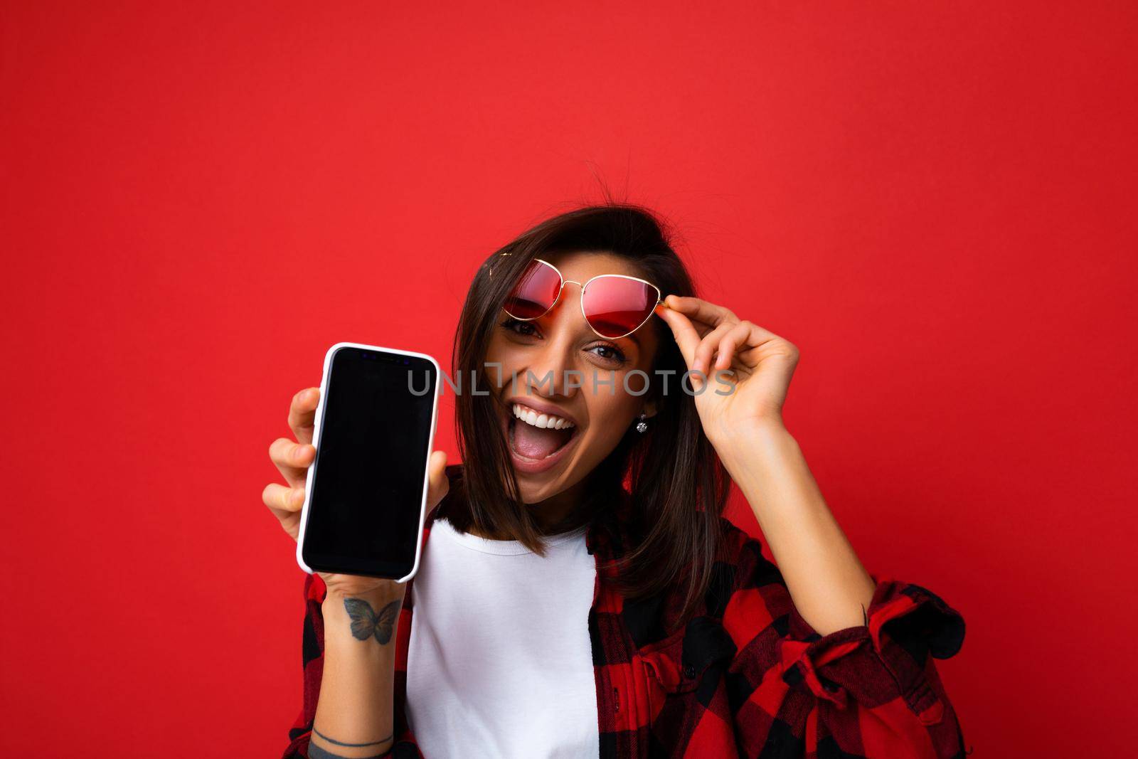 Photo of beautiful smiling young woman good looking wearing casual stylish outfit standing isolated on background with copy space holding smartphone showing phone in hand with empty screen display for mockup looking at camera by TRMK