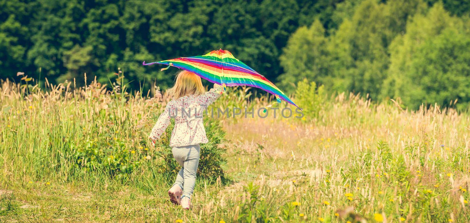 little cute girl flying a kite in a meadow on a sunny day, back view