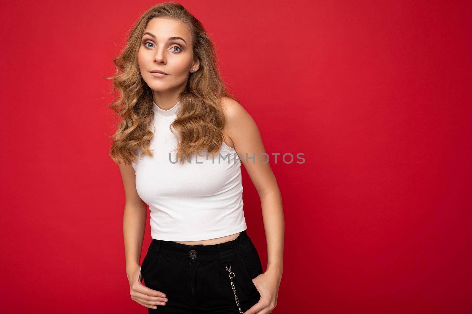 Portrait photo of young beautiful pretty self-confident assertive cool blonde woman with sincere emotions wearing stylish white top isolated over red background with free space.