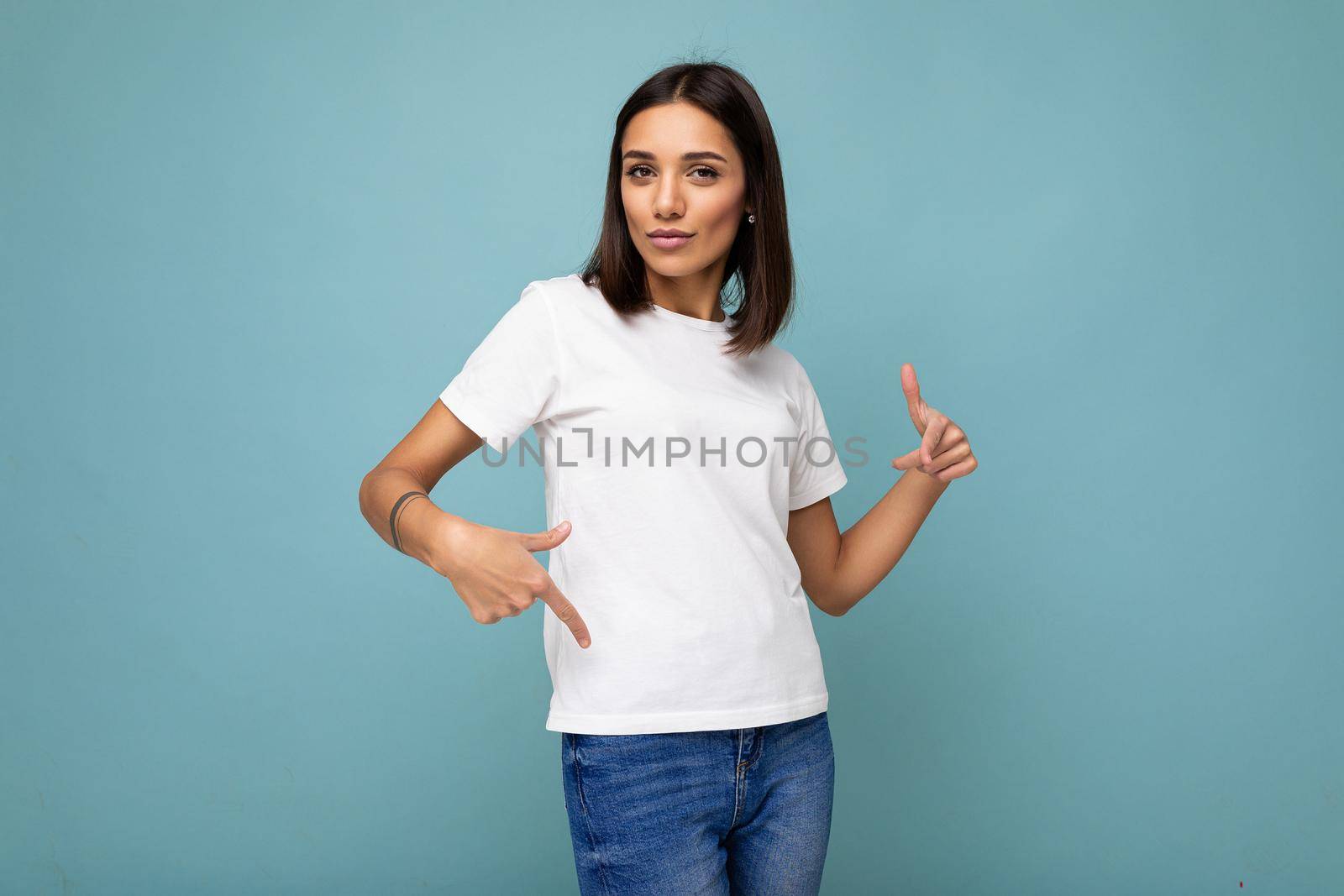 Attractive self-confident young brunette woman in casual white t-shirt for mockup isolated on blue background with free space by TRMK