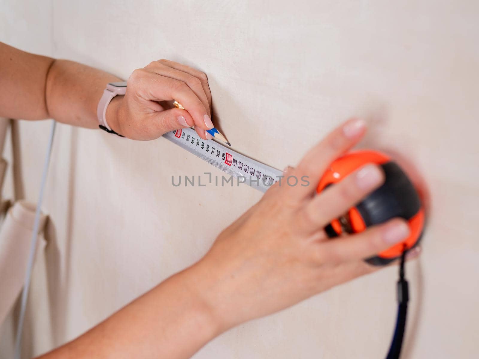 A woman makes a measurement on the wall in a room using a measuring tape.