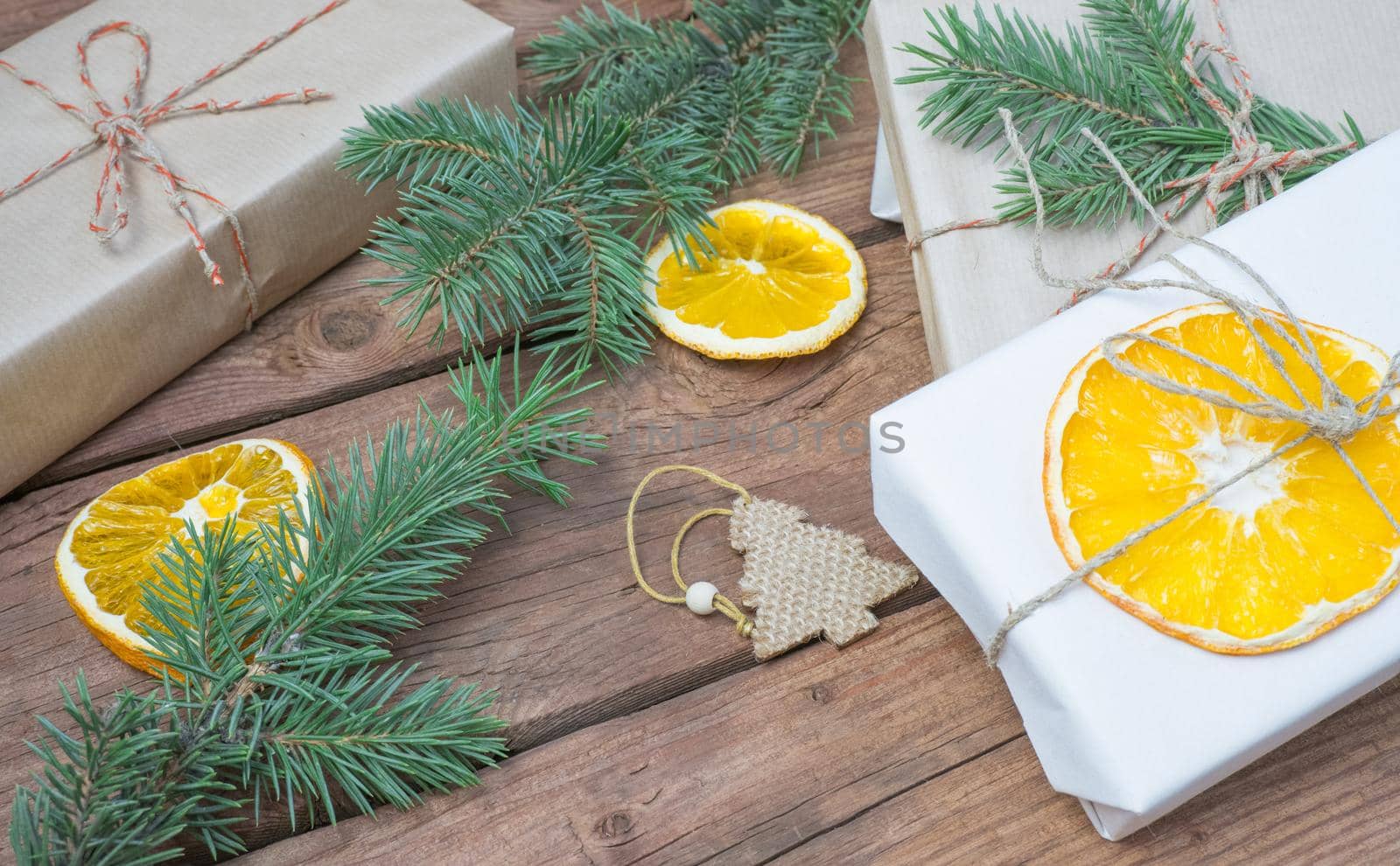 Christmas gifts or gift box wrapped in kraft paper with decorations, pine cones and fir branches on a rustic wooden background.