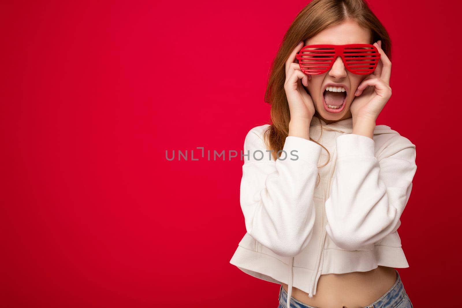 Photo shot of beautiful positive young blonde woman wearing casual clothes and stylish optical glasses isolated over colorful background wall looking at camera and having fun by TRMK