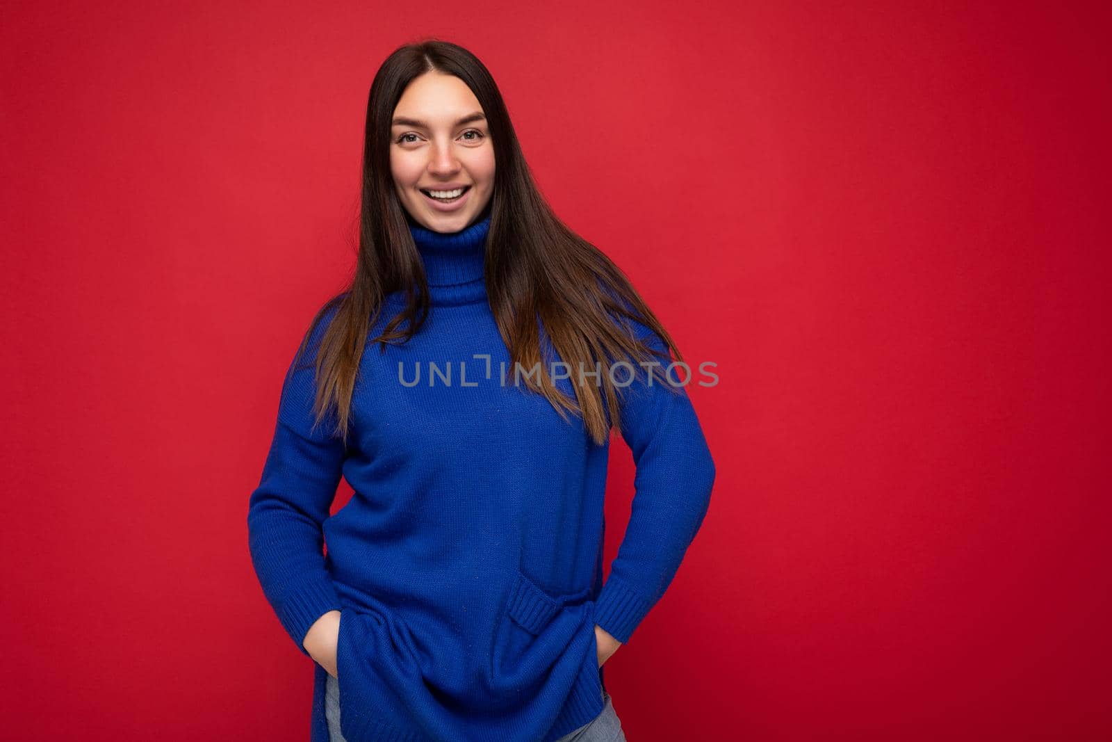 Happy young beautiful brunette female person with sincere emotions isolated on background wall with copy space wearing casual trendy blue sweater. Positive concept by TRMK