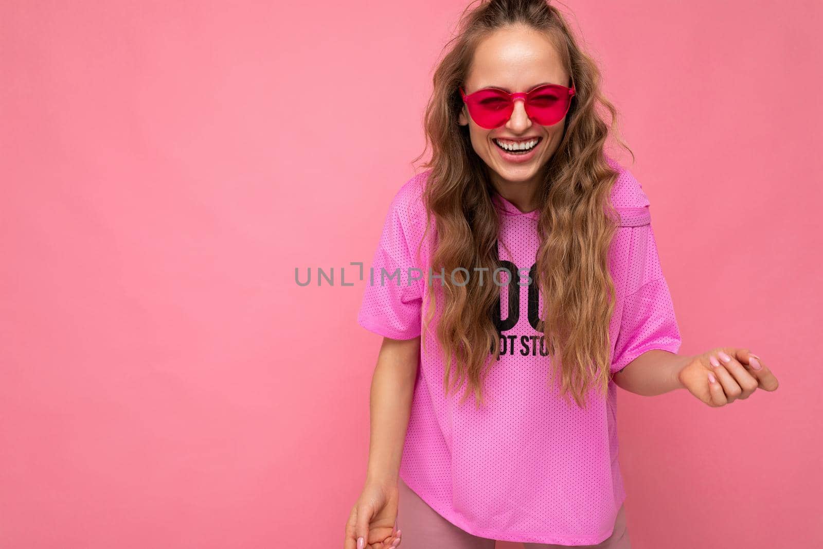 Photo shot of beautiful happy smiling young dark blonde woman wearing casual clothes and stylish sunglasses isolated over colorful background looking at camera by TRMK