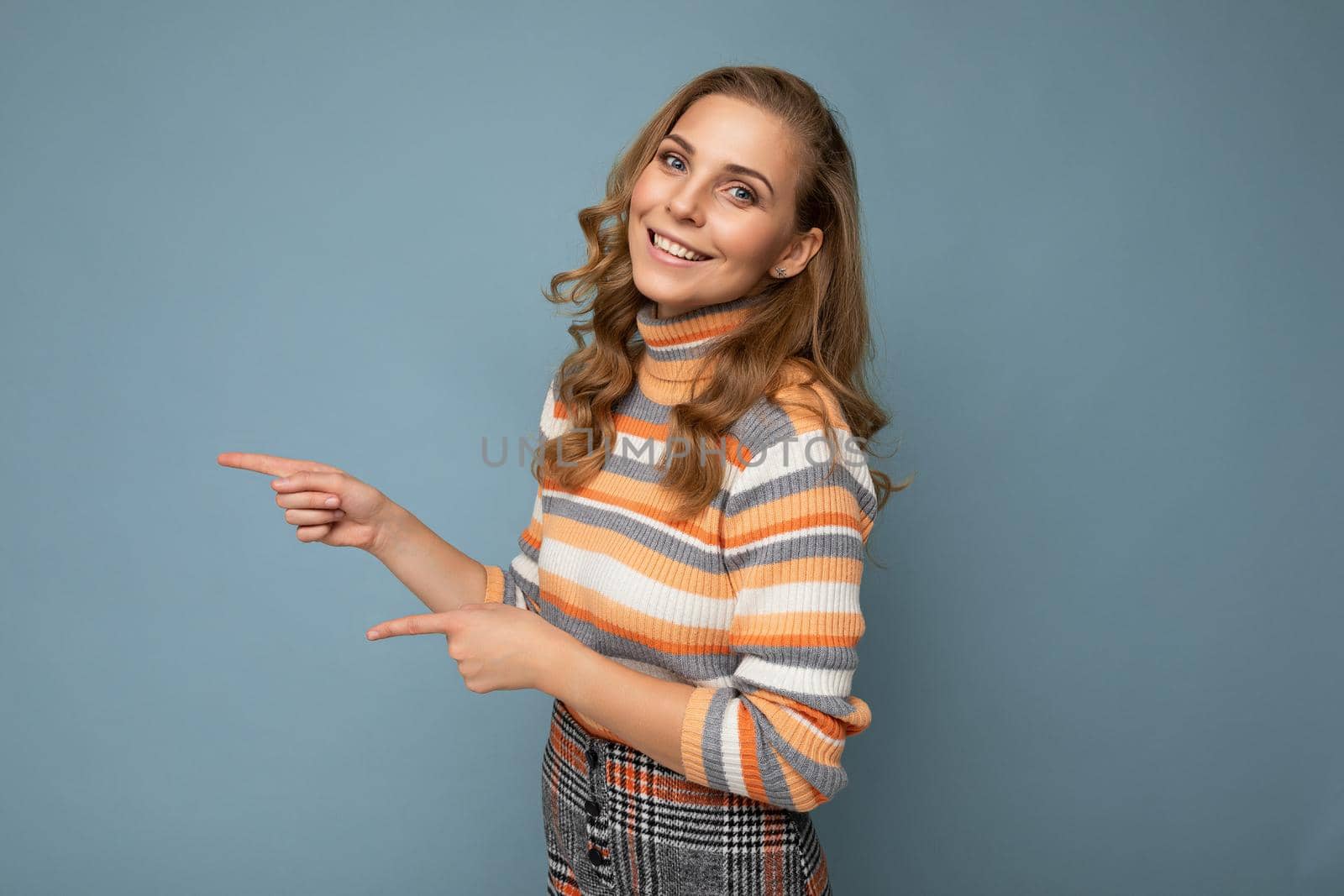 Photo of young positive happy smiling beautiful woman with sincere emotions wearing stylish clothes isolated over background with copy space and pointing at free space for text.