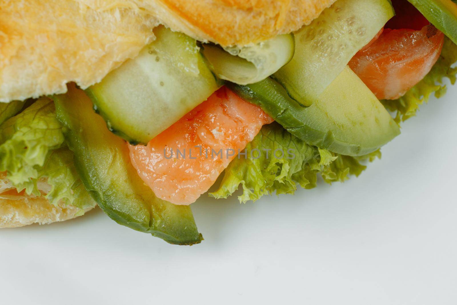 Croissant sandwich with red fish, avocado, fresh vegetables and arugula on black shale board over black stone background. Healthy food concept by UcheaD