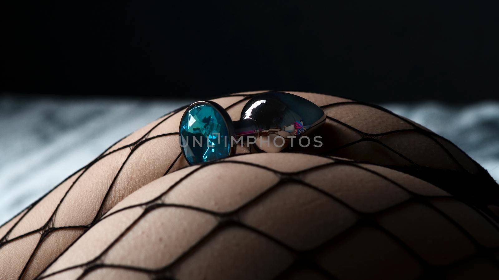 Close-up of anal plug sexy device with blue crystal on the female ass in pantyhose in the fishnet. Adult sex game