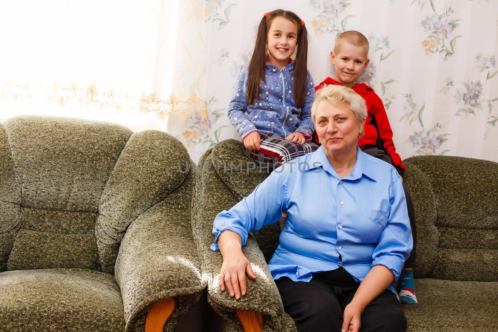 Grandmother and grandchildren sitting together on sofa in living room by Andelov13