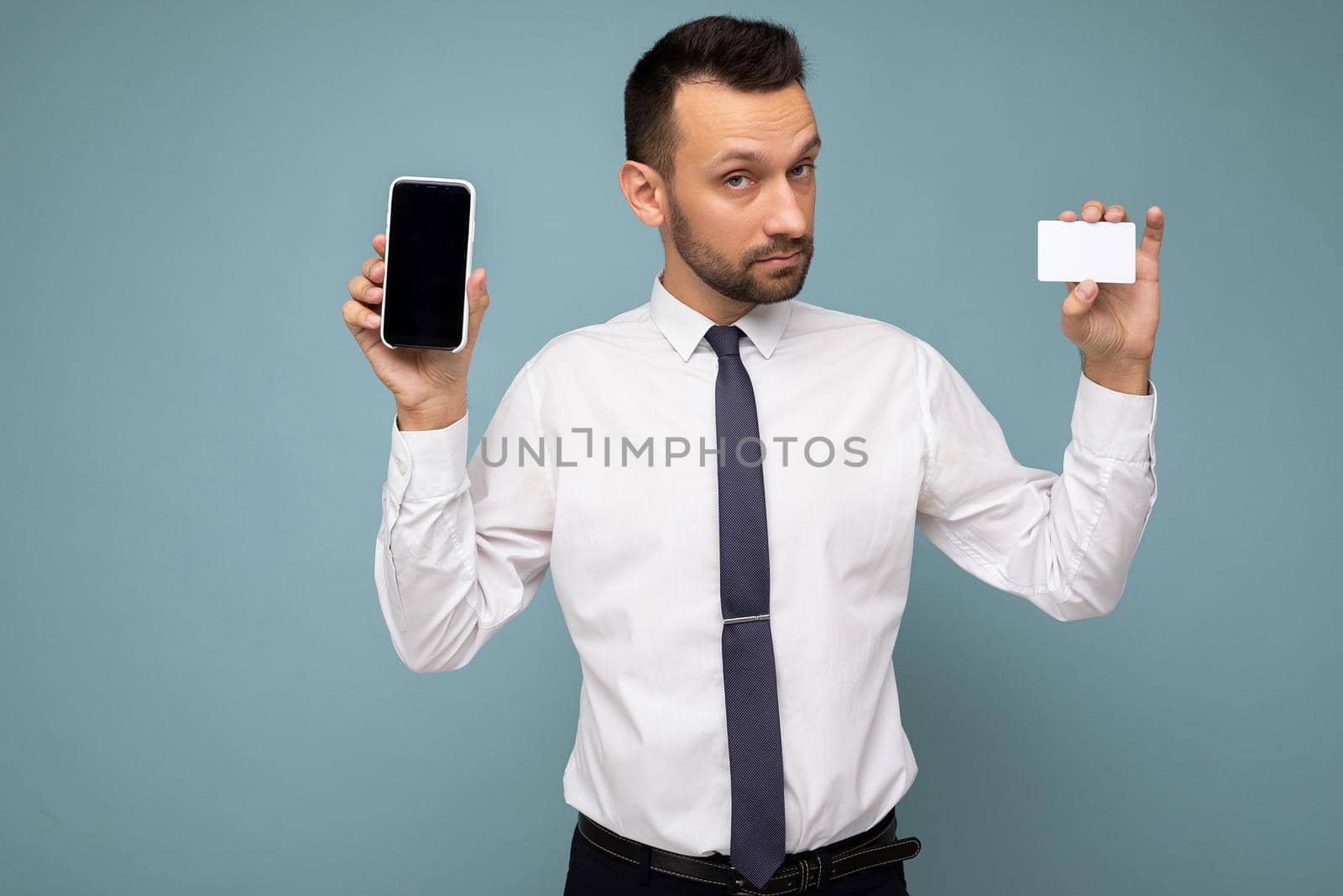 Handsome man wearing everyday clothes isolated on background wall holding and using phone and credit card making payment looking at camera.