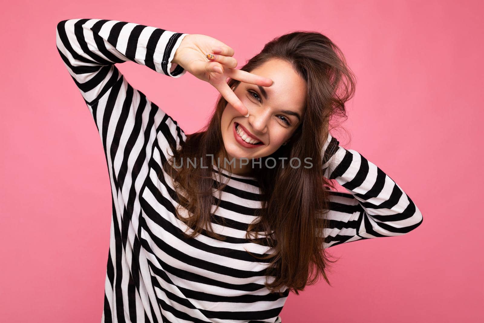 Photo of young european positive smiling winsome happy attractive brunette woman with sincere emotions wearing casual striped pullover isolated on pink background with copy space.